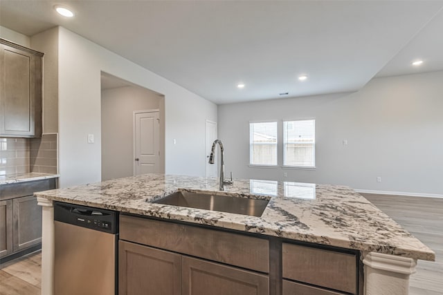 kitchen featuring light stone countertops, light wood-type flooring, tasteful backsplash, sink, and dishwasher