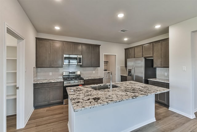 kitchen with sink, backsplash, dark brown cabinets, a center island with sink, and appliances with stainless steel finishes