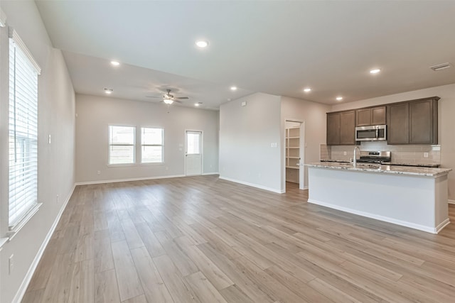 kitchen featuring decorative backsplash, light stone countertops, stainless steel appliances, and light hardwood / wood-style flooring