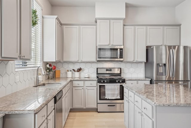 kitchen featuring backsplash, light stone countertops, sink, and appliances with stainless steel finishes