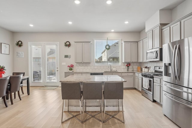 kitchen featuring decorative backsplash, a kitchen breakfast bar, gray cabinetry, stainless steel appliances, and a kitchen island