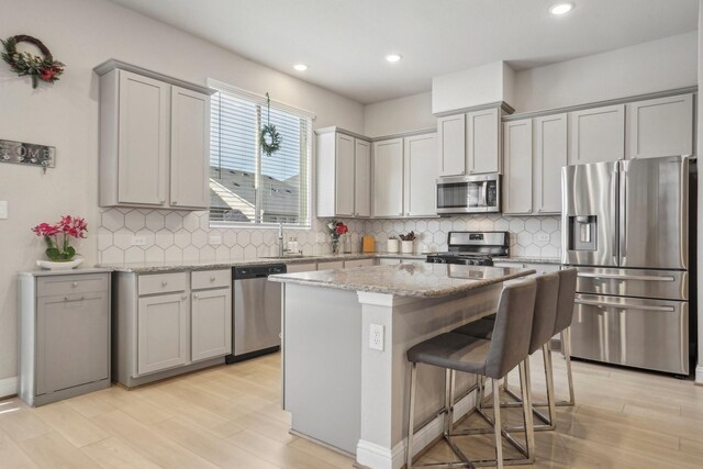 kitchen featuring a center island, stainless steel appliances, light stone counters, a breakfast bar, and light wood-type flooring