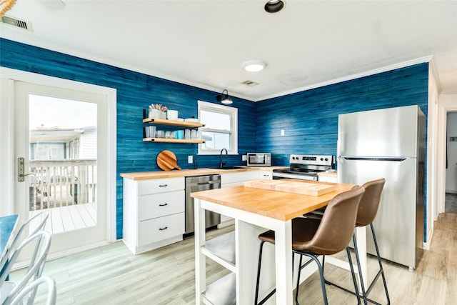 kitchen featuring appliances with stainless steel finishes, crown molding, sink, white cabinets, and light hardwood / wood-style floors