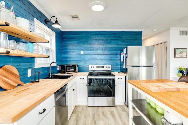 kitchen featuring appliances with stainless steel finishes, ornamental molding, sink, white cabinets, and butcher block countertops