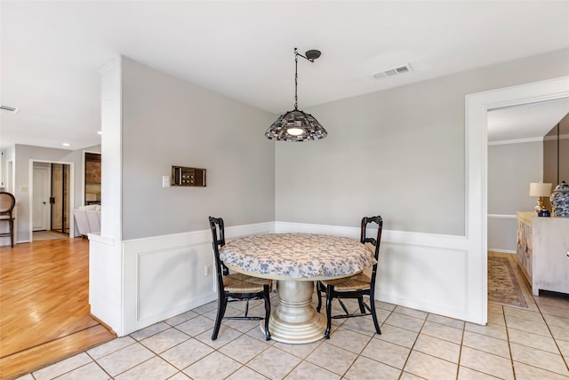 dining room with wainscoting, light tile patterned flooring, visible vents, and a decorative wall