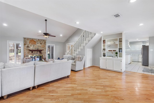 living room featuring stairs, a stone fireplace, light wood finished floors, and visible vents