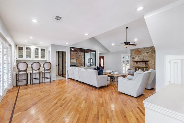 living room featuring visible vents, vaulted ceiling, a stone fireplace, ceiling fan, and light wood-type flooring