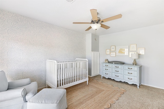 bedroom featuring ceiling fan, light carpet, baseboards, a nursery area, and wallpapered walls