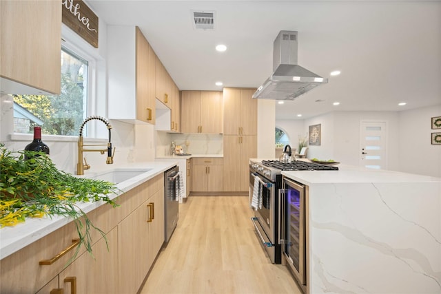 kitchen with sink, wall chimney range hood, stainless steel appliances, and light brown cabinetry