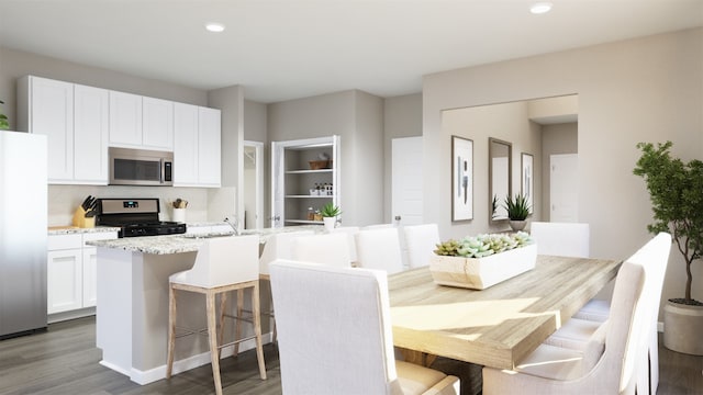 kitchen with a kitchen bar, appliances with stainless steel finishes, light stone countertops, white cabinets, and an island with sink