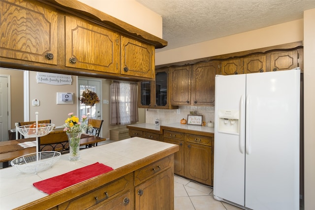 kitchen featuring white refrigerator with ice dispenser, backsplash, tile countertops, a textured ceiling, and light tile patterned floors