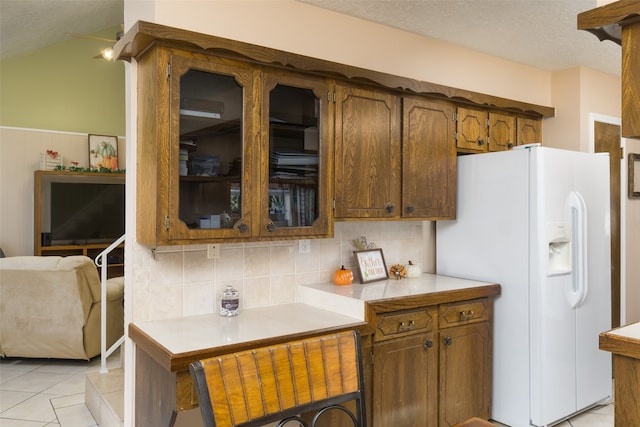 kitchen featuring light tile patterned flooring, white refrigerator with ice dispenser, a textured ceiling, and tasteful backsplash