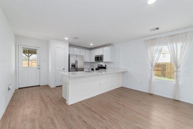 kitchen with white cabinetry, kitchen peninsula, appliances with stainless steel finishes, and light hardwood / wood-style flooring