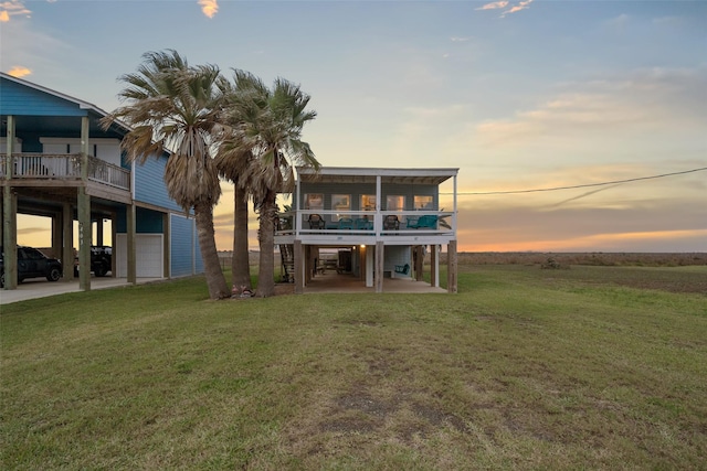 back house at dusk with a balcony, a garage, and a lawn