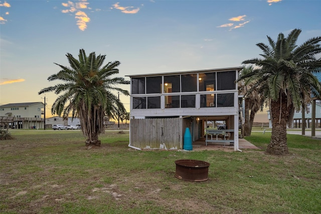 back house at dusk featuring a lawn and a sunroom