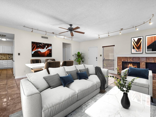 living room with a tile fireplace, ceiling fan, light tile patterned floors, and a textured ceiling