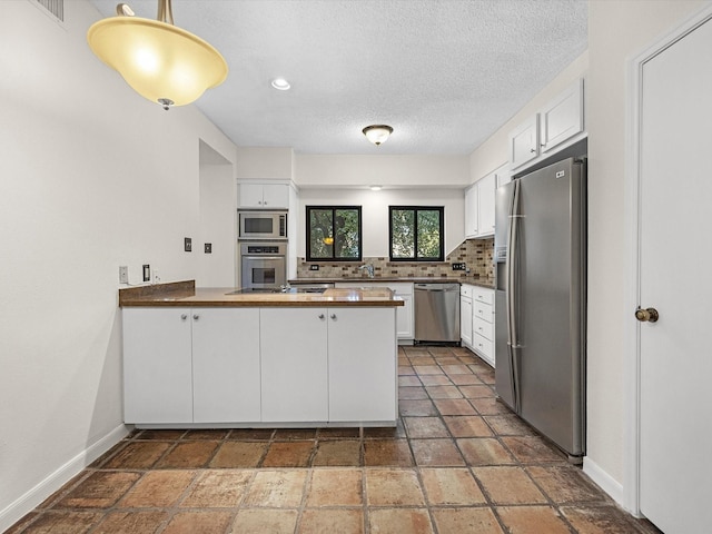 kitchen with white cabinetry, stainless steel appliances, tasteful backsplash, kitchen peninsula, and decorative light fixtures