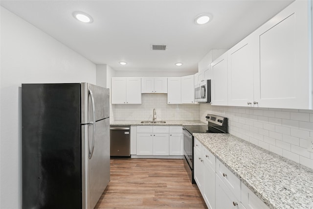 kitchen with sink, backsplash, light hardwood / wood-style floors, white cabinets, and appliances with stainless steel finishes