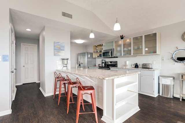 kitchen with stainless steel appliances, a kitchen breakfast bar, pendant lighting, lofted ceiling, and white cabinets