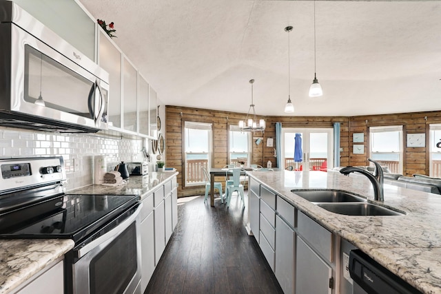 kitchen with appliances with stainless steel finishes, wooden walls, sink, decorative light fixtures, and dark hardwood / wood-style floors