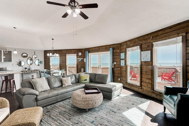 living room with ceiling fan with notable chandelier, lofted ceiling, and wooden walls