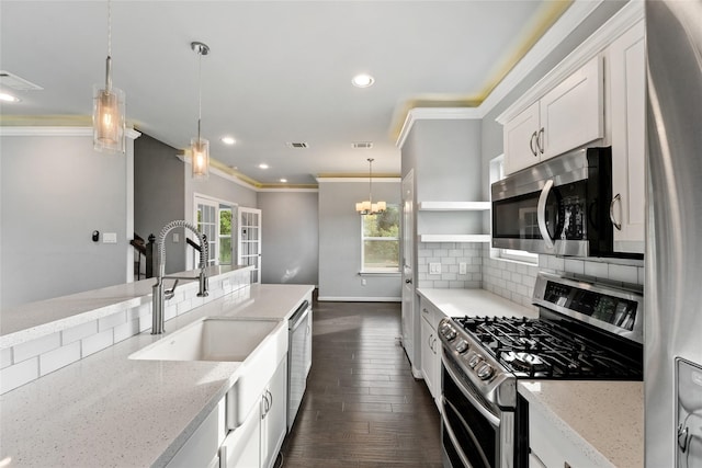 kitchen featuring white cabinets, light stone countertops, ornamental molding, appliances with stainless steel finishes, and decorative light fixtures