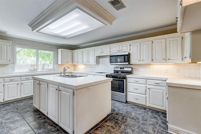 kitchen with sink, stainless steel appliances, tile countertops, an island with sink, and white cabinets