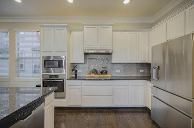 kitchen with white cabinets, appliances with stainless steel finishes, backsplash, and dark stone counters