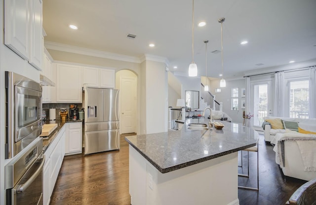 kitchen with a kitchen island with sink, hanging light fixtures, dark hardwood / wood-style floors, appliances with stainless steel finishes, and white cabinetry