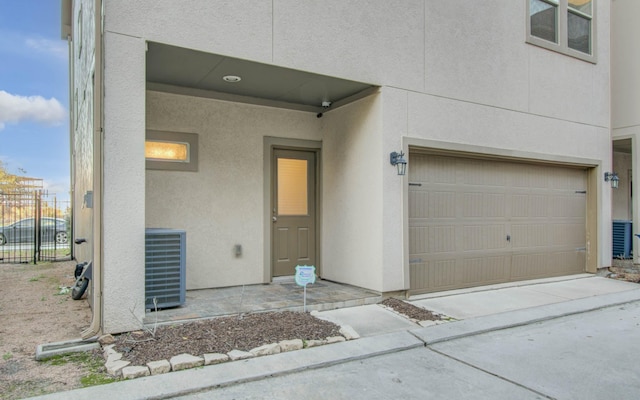 view of exterior entry with central AC unit and a garage