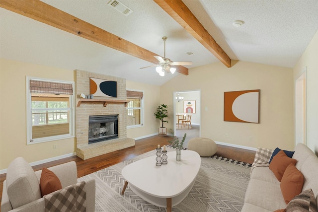 living room with a textured ceiling, ceiling fan, wood-type flooring, lofted ceiling with beams, and a fireplace