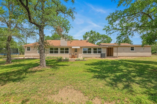 rear view of property with a yard and a trampoline