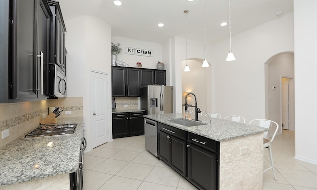 kitchen featuring light stone countertops, hanging light fixtures, decorative backsplash, a kitchen island with sink, and appliances with stainless steel finishes