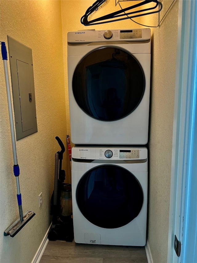 laundry area with electric panel, stacked washing maching and dryer, and hardwood / wood-style flooring