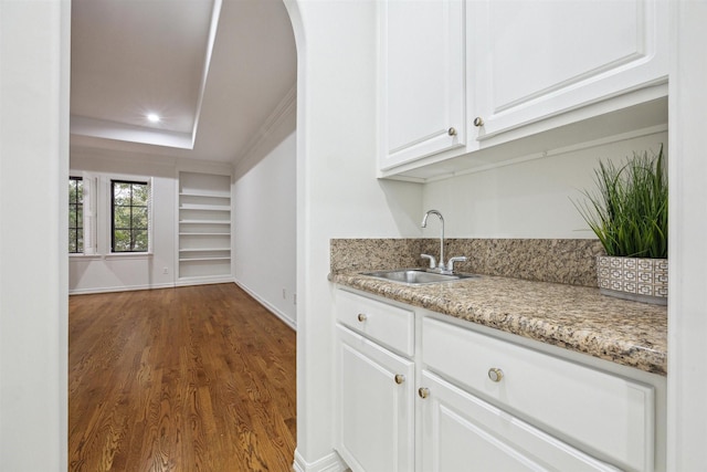 bar with light stone counters, a tray ceiling, dark wood-type flooring, sink, and white cabinetry