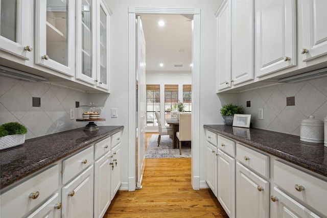 bar featuring backsplash, light wood-type flooring, white cabinetry, and dark stone countertops