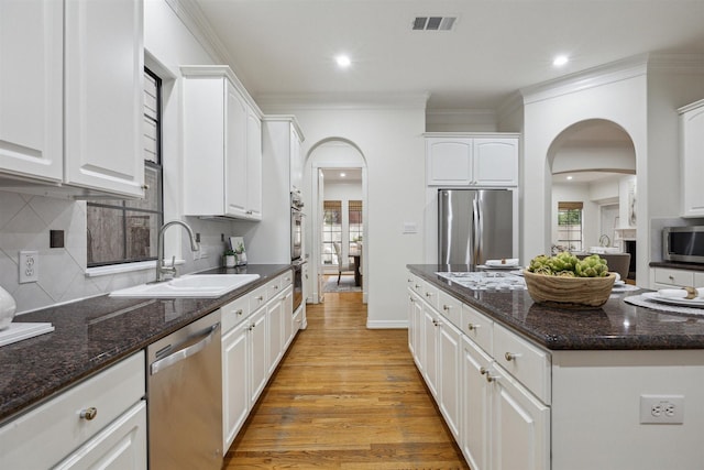 kitchen with appliances with stainless steel finishes, white cabinetry, dark stone counters, and sink