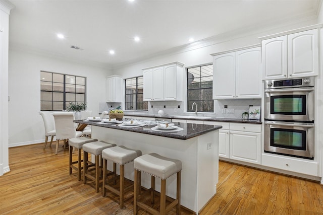 kitchen featuring white cabinets, decorative backsplash, a kitchen island, and double oven