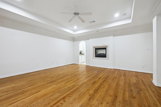 unfurnished living room featuring hardwood / wood-style floors, ceiling fan, a raised ceiling, and ornamental molding