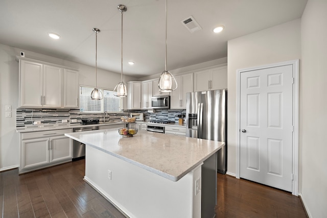 kitchen featuring light stone countertops, stainless steel appliances, decorative light fixtures, white cabinets, and a kitchen island