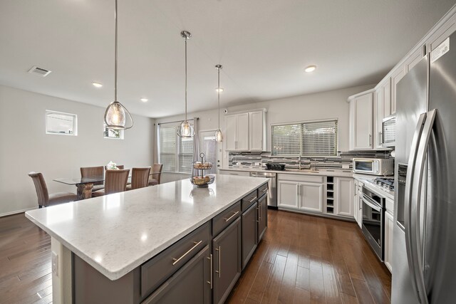 kitchen with a center island, white cabinets, decorative light fixtures, and appliances with stainless steel finishes