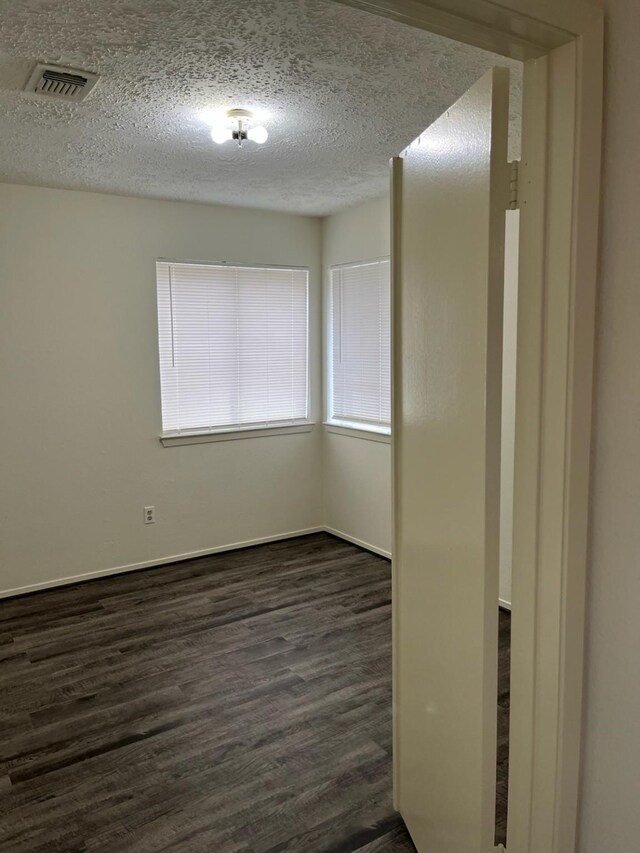 spare room featuring a textured ceiling and dark hardwood / wood-style floors