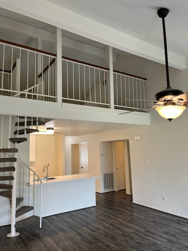 unfurnished living room with sink, a towering ceiling, and dark wood-type flooring