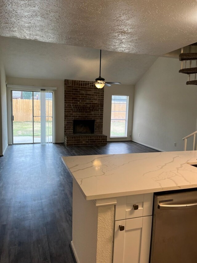 kitchen featuring dishwasher, a fireplace, a textured ceiling, light stone counters, and white cabinetry