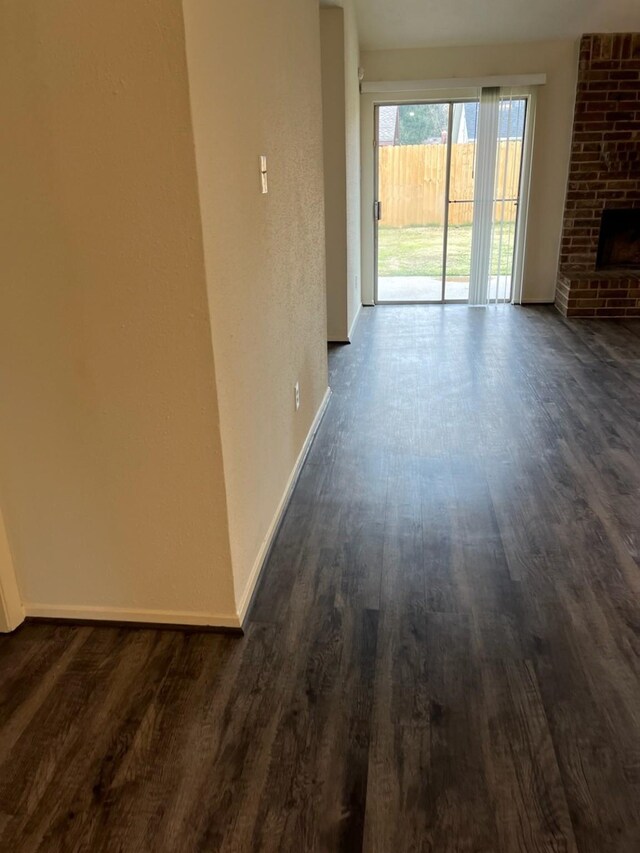 unfurnished living room featuring dark wood-type flooring and a brick fireplace