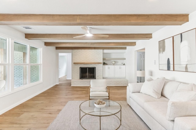 living room with ceiling fan, beamed ceiling, light wood-type flooring, and a brick fireplace