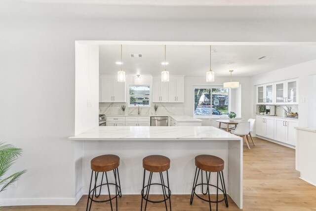 kitchen featuring a kitchen breakfast bar, tasteful backsplash, stainless steel appliances, pendant lighting, and white cabinetry