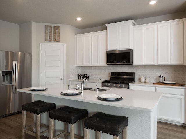 kitchen with sink, stainless steel appliances, wood-type flooring, a center island with sink, and white cabinets