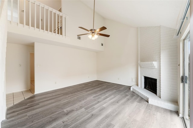 unfurnished living room featuring wood-type flooring, high vaulted ceiling, a brick fireplace, and ceiling fan