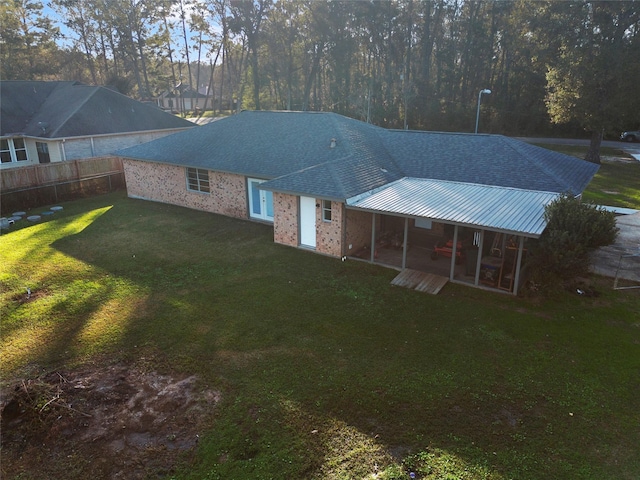 rear view of house featuring brick siding, a yard, a sunroom, metal roof, and fence